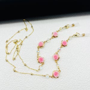 May include: Gold chain with pink rose accents and clear beads. The chain has two loops at each end for attaching to glasses.
