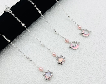 May include: Three silver chains with pink and white celestial charms. The charms are a star, a crescent moon, and a planet with rings. The chains are delicate and would make a great addition to a jewelry collection.