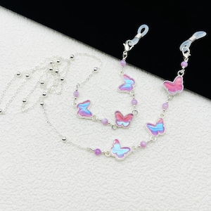 May include: A silver chain with small beads and iridescent butterfly charms. The chain has two clasps for attaching to glasses.