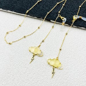 May include: Gold chain with a cloud and lightning bolt charm. The chain is made of small gold beads and has a clear silicone holder for glasses.