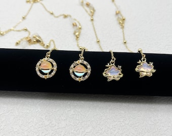 May include: Three gold-tone necklaces with celestial-themed pendants. The pendants feature a planet, a star, and a cloud, all with iridescent finishes and surrounded by small sparkling stones.