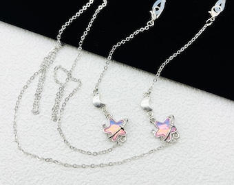 May include: Two silver chains with clear plastic clasps and star-shaped charms. The charms are iridescent and have a crescent moon design.