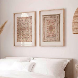 May include: Two framed, vintage-style wall art pieces with intricate, floral-patterned designs in shades of red, beige, and brown hang above a bed with white linens and a peach-colored throw. A woven pendant light and decorative vase are also visible.