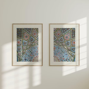 May include: Two framed art prints showcasing a detailed mosaic pattern in shades of blue, teal, pink, and gold. The intricate design is framed in a light wood frame, creating a contrast against the white wall.