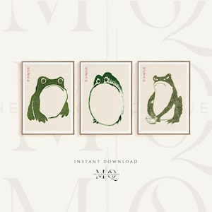 Puede incluir: Tres impresiones enmarcadas con una ilustración de rana verde. Las impresiones tienen un fondo blanco y el texto japonés "おさる" en rojo. La rana de la impresión de la izquierda está sentada con la boca abierta. La rana de la impresión del medio está sentada con las piernas cruzadas. La rana de la impresión de la derecha está sentada con los brazos cruzados y sostiene un tazón.