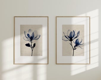 May include: Two framed prints featuring blue floral illustrations. The flowers have a translucent quality, set against a beige background. The frames are a light wood color, adding a natural touch to the artwork. The prints are displayed on a white wall.