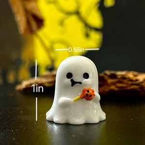 May include: A small, white ghost figurine holding a small orange flower with a yellow stem. The ghost has black eyes and a smiling mouth. The figurine is approximately 1 inch tall and 0.55 inches wide. Halloween decor.