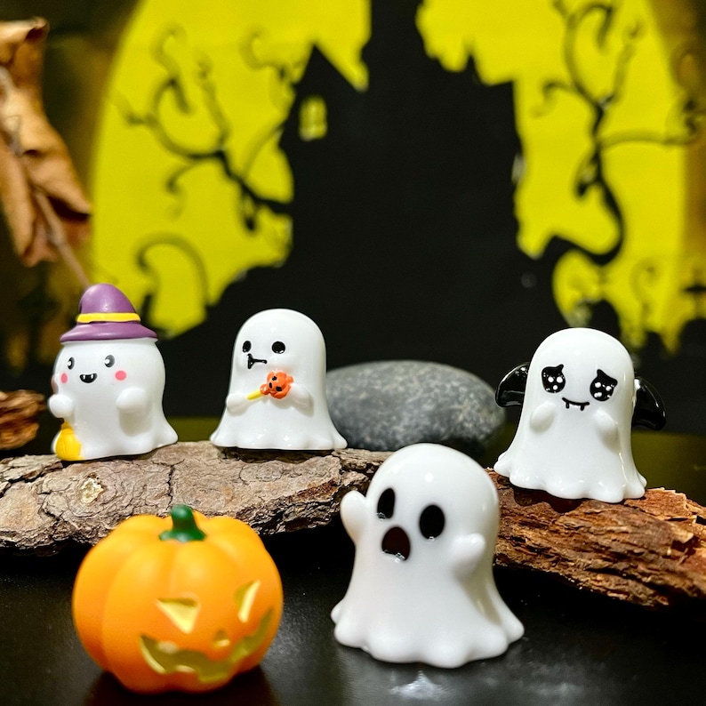 May include: A collection of Halloween-themed figurines, including white ghosts with various expressions, a jack-o'-lantern, and a ghost wearing a witch hat. The background features a yellow moon and a silhouette of a haunted house.