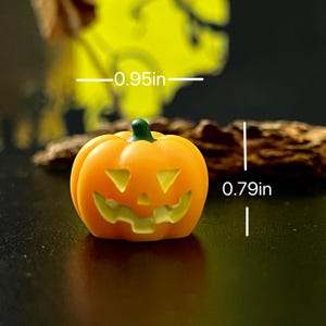 May include: A small, orange pumpkin with a carved jack-o'-lantern face. The pumpkin is 0.95 inches wide and 0.79 inches tall, with a green stem. Perfect for Halloween decorations or miniature displays.