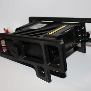 May include: A black AnyTone radio transceiver with a black mounting bracket. The radio has a series of buttons and a knob on the front panel. The bracket has a rectangular shape with cutouts.
