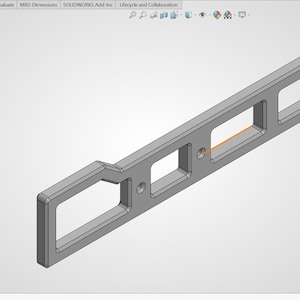 May include: A gray, rectangular metal component with three rectangular cutouts and two circular holes. The component has a handle-like extension on one end. The design appears to be a 3D model or technical drawing.