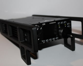 May include: A black G90 HF transceiver radio with multiple knobs and buttons, mounted in a black frame. The radio has a small screen and an antenna. The frame has a handle on the side and is supported by two legs.