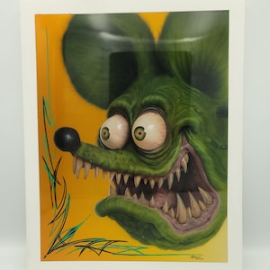 May include: Framed artwork featuring a green, cartoonish rat with bulging eyes and a wide, toothy grin. The rat has a black nose and large ears. The background is yellow with green and black pinstripes.