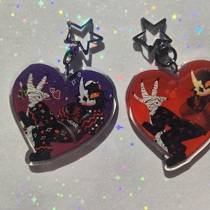 May include: Two heart-shaped acrylic charms. One is purple with a white and black character design, the other is red with a similar character. Both have a star-shaped clasp. The charms feature the text "GIRLS WEAR".