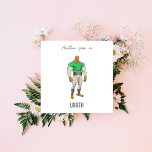 May include: A square greeting card featuring the text "Another year on" above a cartoon illustration of a muscular character in a green and white uniform. The character is labeled "URATH" below. The card is surrounded by pink flowers and greenery.