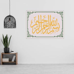 Op de afbeelding: Een ingelijst kunstwerk met gele Arabische kalligrafie tegen een lichtroze achtergrond. De kalligrafie is omlijst door een groene rand met decoratieve bloemelementen. Het kunstwerk wordt tentoongesteld op een witte muur.