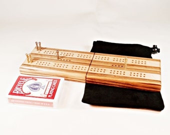 Könnte beinhalten: Ein hölzernes Cribbage-Brett mit zwei Spielflächen, Messing-Stiften und einer schwarzen Tragetasche. Ein Deck Bicycle-Spielkarten ist ebenfalls enthalten.