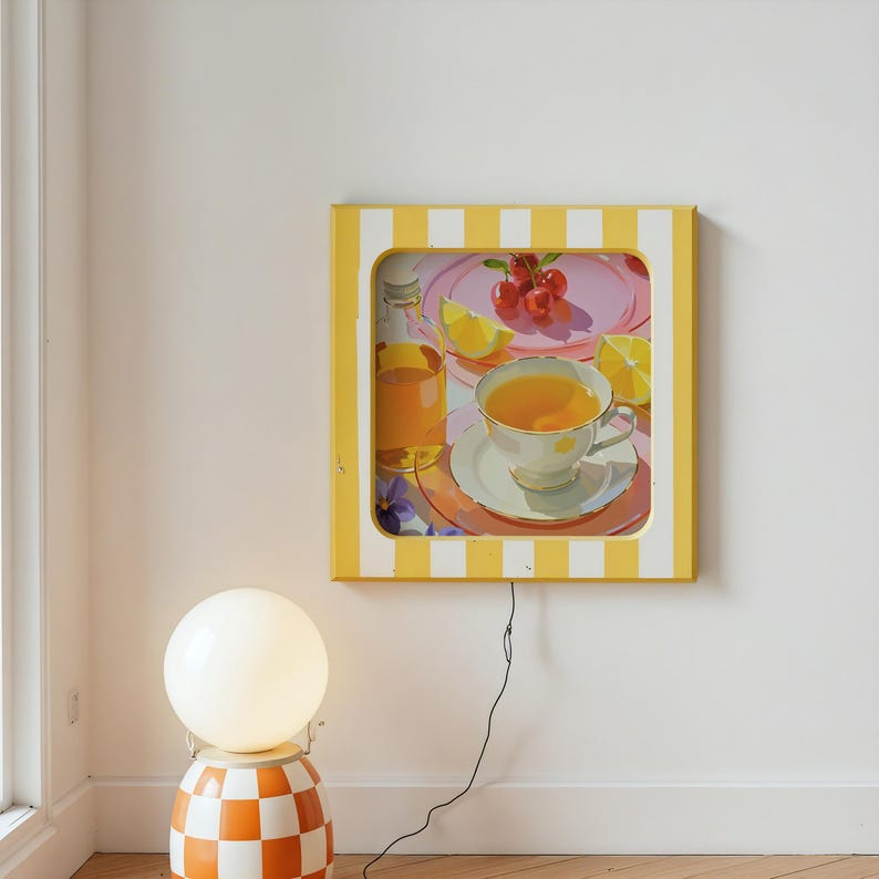 May include: A framed artwork with a yellow and white striped border depicts a still life of a tea setting. The painting includes a teacup, cherries, lemon slices, and a glass of juice. A round, white globe lamp sits on a checkered orange and white base.