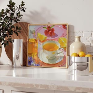 May include: A framed print of a still life with a teacup, cherries, and lemons. A silver vase and a bowl of lemons are on the counter. A bottle of liquid is next to the print. The color palette is soft and pastel.