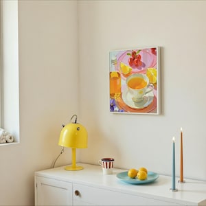 May include: A yellow desk lamp with a curved handle sits on a white cabinet. A framed painting of a tea setting with cherries and lemons hangs on the wall. A blue plate holds lemons, and two candles stand nearby.