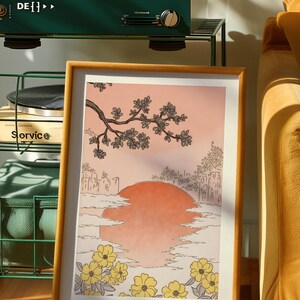 Puede incluir: Una impresi&oacute;n enmarcada de una ilustraci&oacute;n de inspiraci&oacute;n japonesa que presenta una puesta de sol estilizada sobre un horizonte urbano con una rama de cerezos en flor en primer plano. La impresi&oacute;n tiene un fondo melocot&oacute;n y flores amarillas.