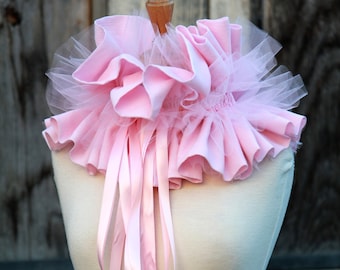 May include: A pink ruffled collar with a tulle overlay and matching satin ribbons tied in knots. The collar is displayed on a white mannequin.