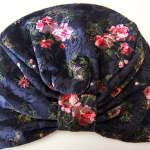 Puede incluir: Un turbante de encaje negro con un patr&oacute;n floral en tonos de rosa y verde.