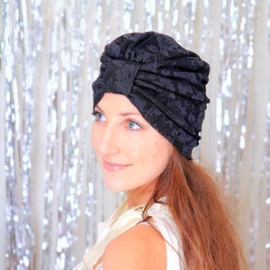 May include: A black turban with a floral pattern. The turban is made of a soft, stretchy fabric and is designed to be comfortable to wear. The turban is a stylish and versatile accessory that can be worn for a variety of occasions.