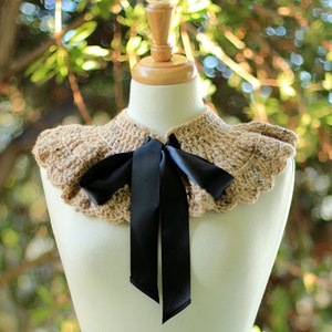 May include: A crocheted collar with a ruffled edge in a beige and brown color. A black satin ribbon is tied in a bow at the center of the collar.