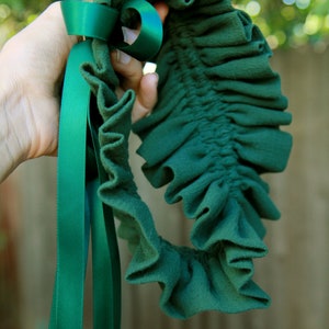May include: A green fabric garter with a green satin ribbon tied in a bow. The garter is ruffled and has a gathered elastic band.