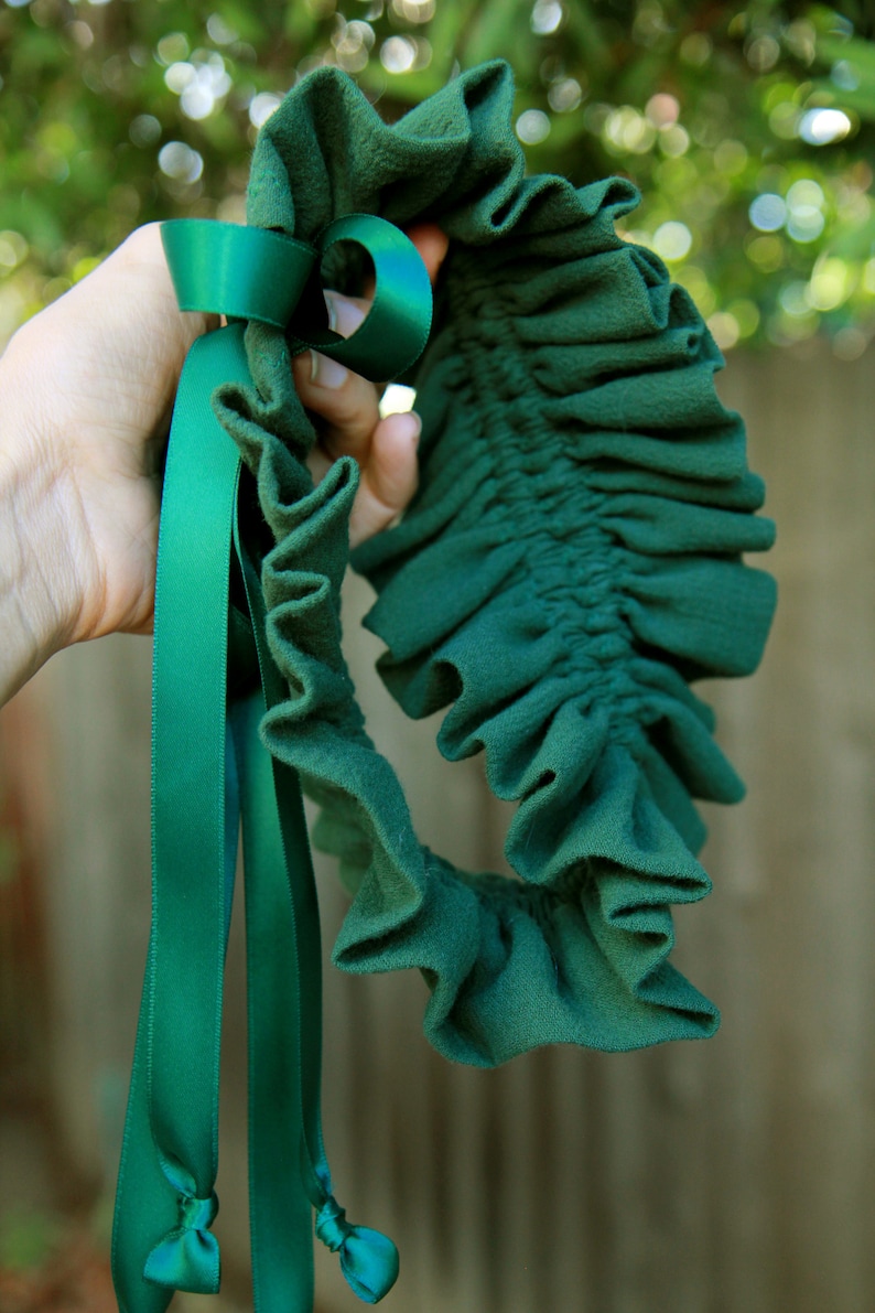 May include: A green fabric garter with a green satin ribbon tied in a bow. The garter is ruffled and has a gathered elastic band.