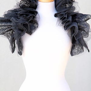 May include: A black lace collar with a ruffled design. The collar is displayed on a white mannequin.