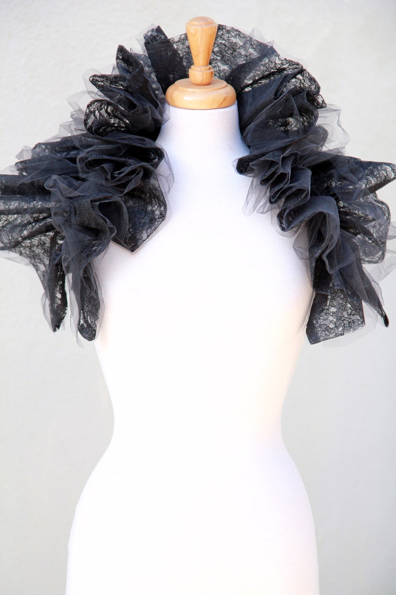 May include: A black lace collar with a ruffled design. The collar is displayed on a white mannequin.