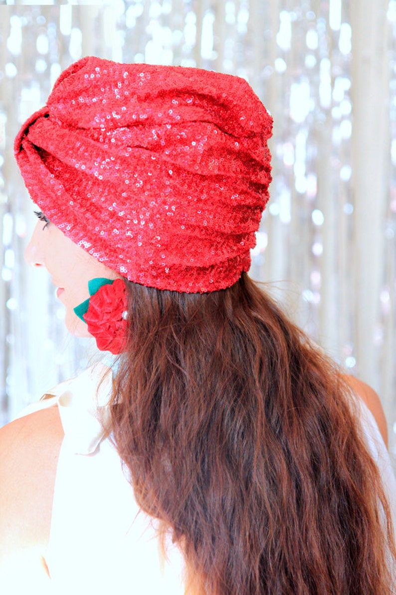Puede incluir: Un turbante rojo de lentejuelas con un acento de flor roja. El turbante lo lleva una persona con el pelo largo y casta&ntilde;o.