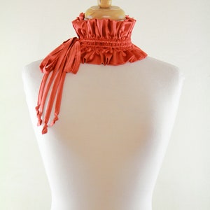 May include: A red ruffled collar with a long, thin tie. The collar is made of a soft, silky fabric and is perfect for adding a touch of elegance to any outfit.