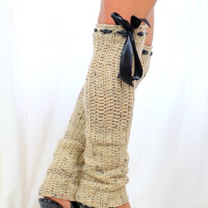May include: Beige crochet leg warmers with a black satin ribbon bow. The leg warmers are worn with black platform heels.