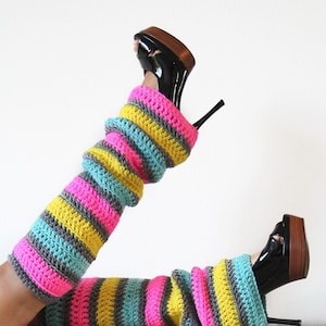 May include: A pair of colorful striped leg warmers made of crochet yarn. The leg warmers are pink, yellow, gray, and teal. The leg warmers are worn with black high-heeled shoes.