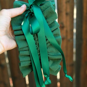 May include: A green fabric garter with a green satin ribbon tied in a bow. The ribbon has long tails that are tied in knots at the ends.
