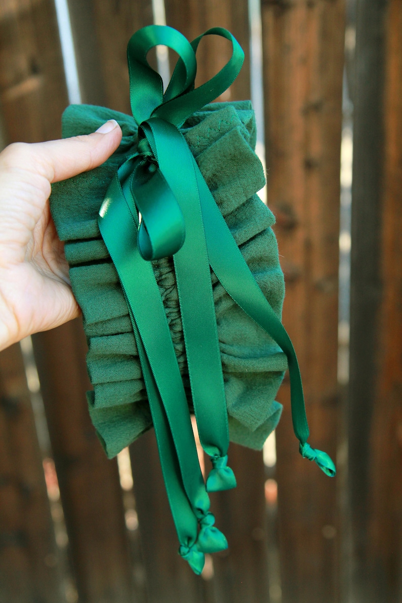 May include: A green fabric garter with a green satin ribbon tied in a bow. The ribbon has long tails that are tied in knots at the ends.