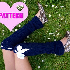 Peut inclure: Une paire de jambières en crochet bleu avec des nœuds blancs sur les côtés. Les jambières sont portées par une personne assise dans un champ herbeux.