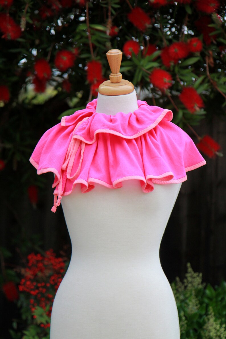 May include: A pink ruffled collar with a white trim, displayed on a white mannequin.