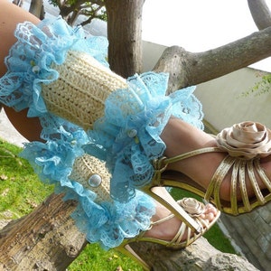 May include: A pair of light blue lace leg warmers with a crocheted cream fabric. The leg warmers are worn with gold high-heeled sandals with a large brown fabric flower.