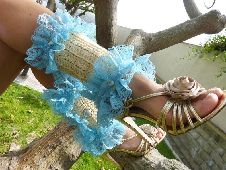 May include: A pair of light blue lace leg warmers with a crocheted cream fabric. The leg warmers are worn with gold high-heeled sandals with a large brown fabric flower.