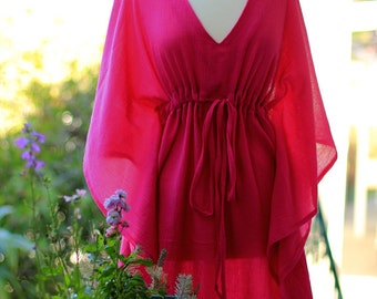 May include: A pink, flowing kaftan dress with a V-neckline and a drawstring waist. The dress is made of a lightweight fabric and has a relaxed fit.