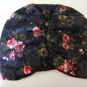 Puede incluir: Un turbante de encaje negro con un patr&oacute;n floral con rosas rosas y verdes.