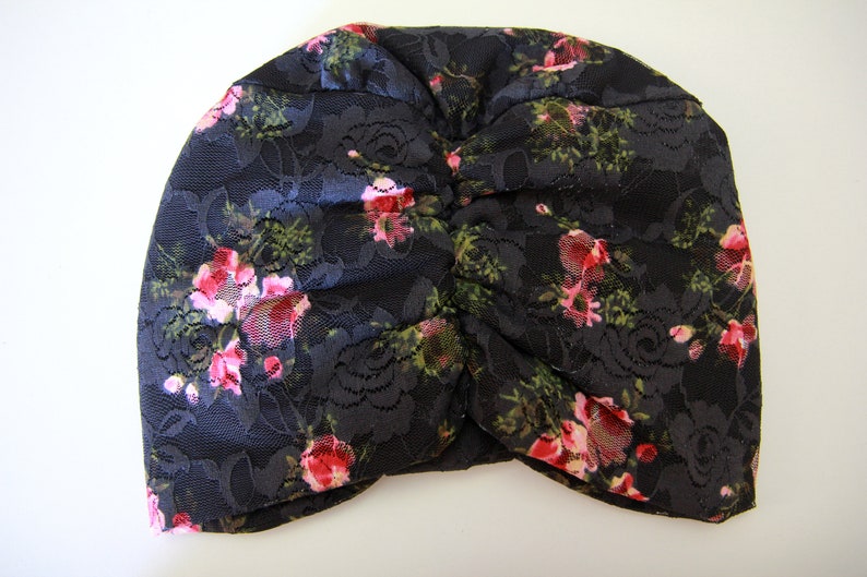 Puede incluir: Un turbante de encaje negro con un patr&oacute;n floral con rosas rosas y verdes.