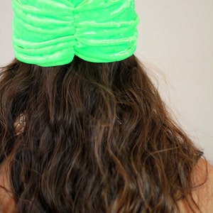 May include: A bright green velvet turban style hat. The hat is gathered and has a smooth, shiny finish.