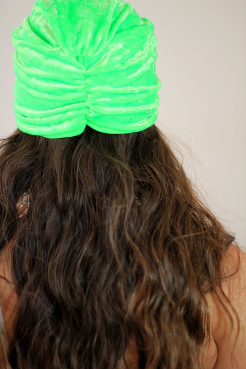 May include: A bright green velvet turban style hat. The hat is gathered and has a smooth, shiny finish.