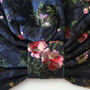 Puede incluir: Tela de encaje negra con un patr&oacute;n floral en tonos de rosa y verde. La tela est&aacute; recogida y atada en un lazo.