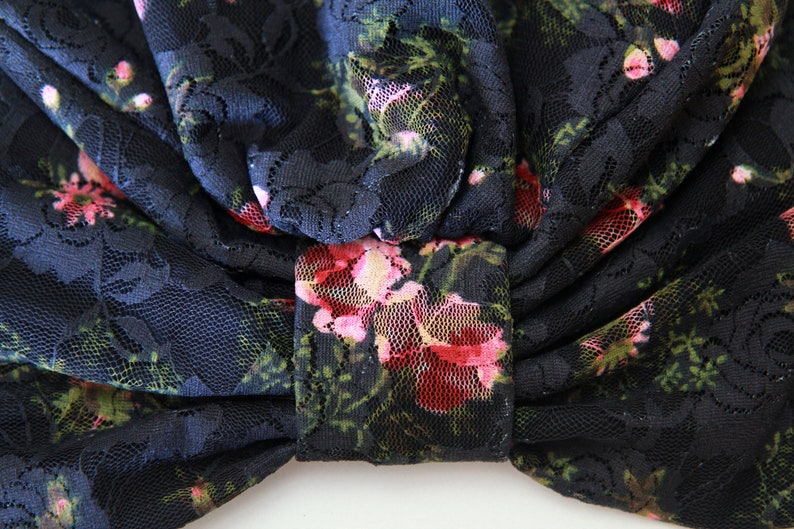 Puede incluir: Tela de encaje negra con un patr&oacute;n floral en tonos de rosa y verde. La tela est&aacute; recogida y atada en un lazo.